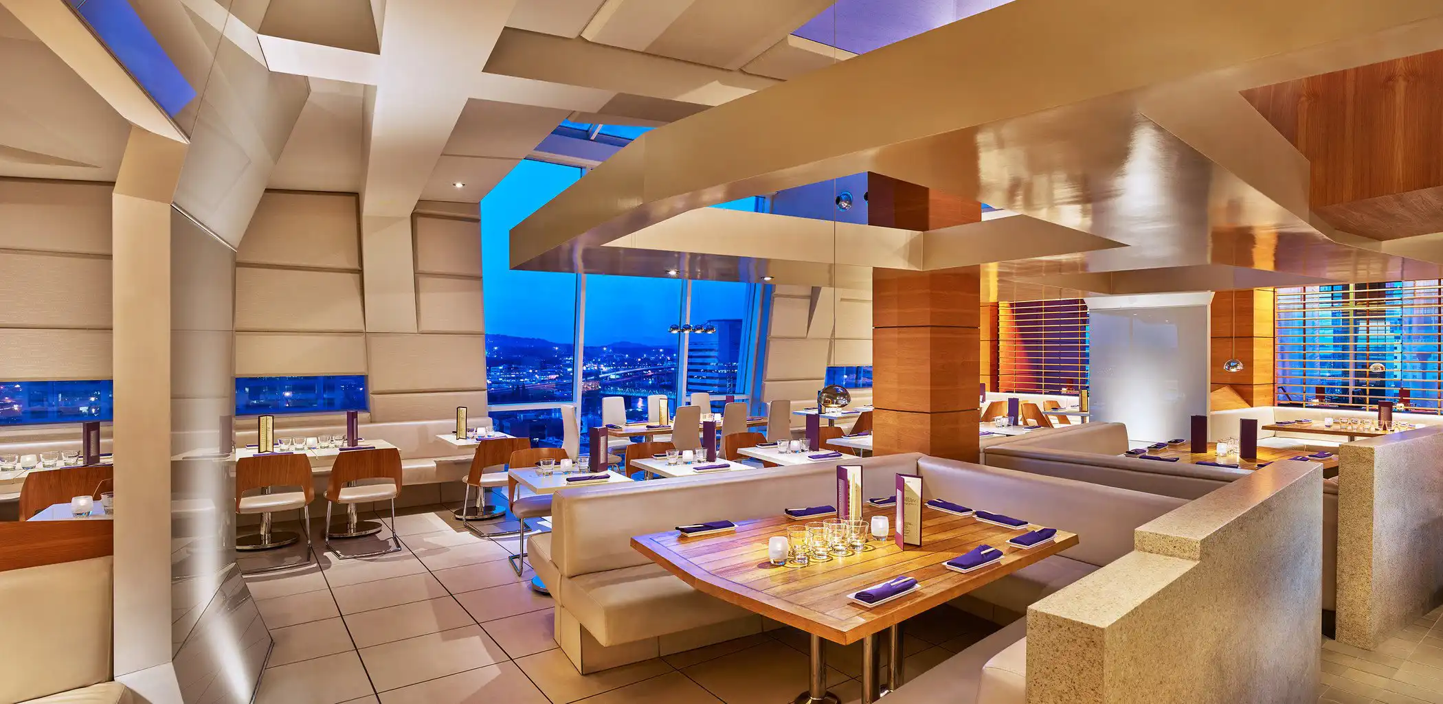 Modern restaurant interior with geometric ceiling and city views at night