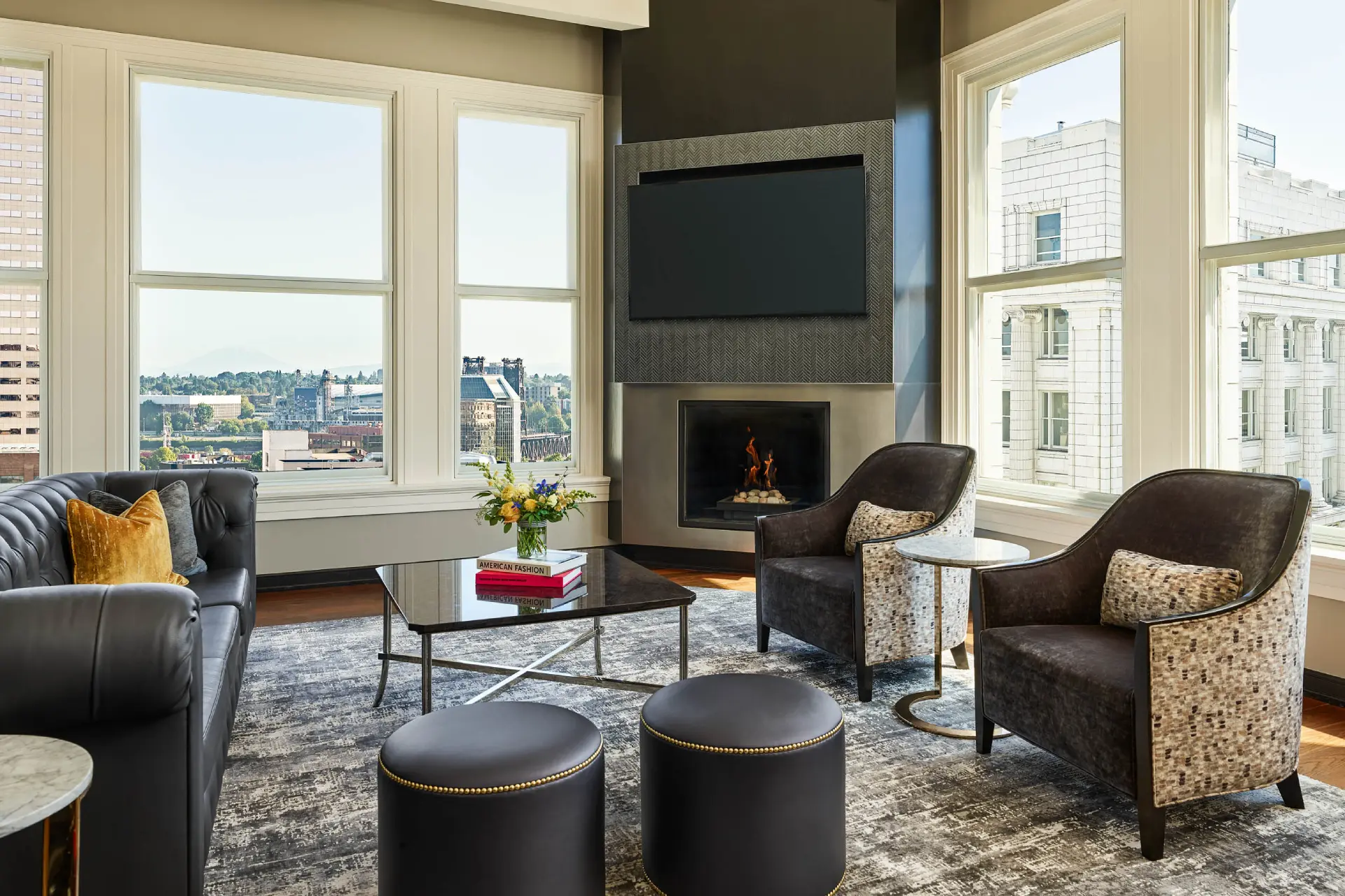 A sophisticated hotel suite living room featuring a fireplace, plush seating, and expansive views of downtown Portland.