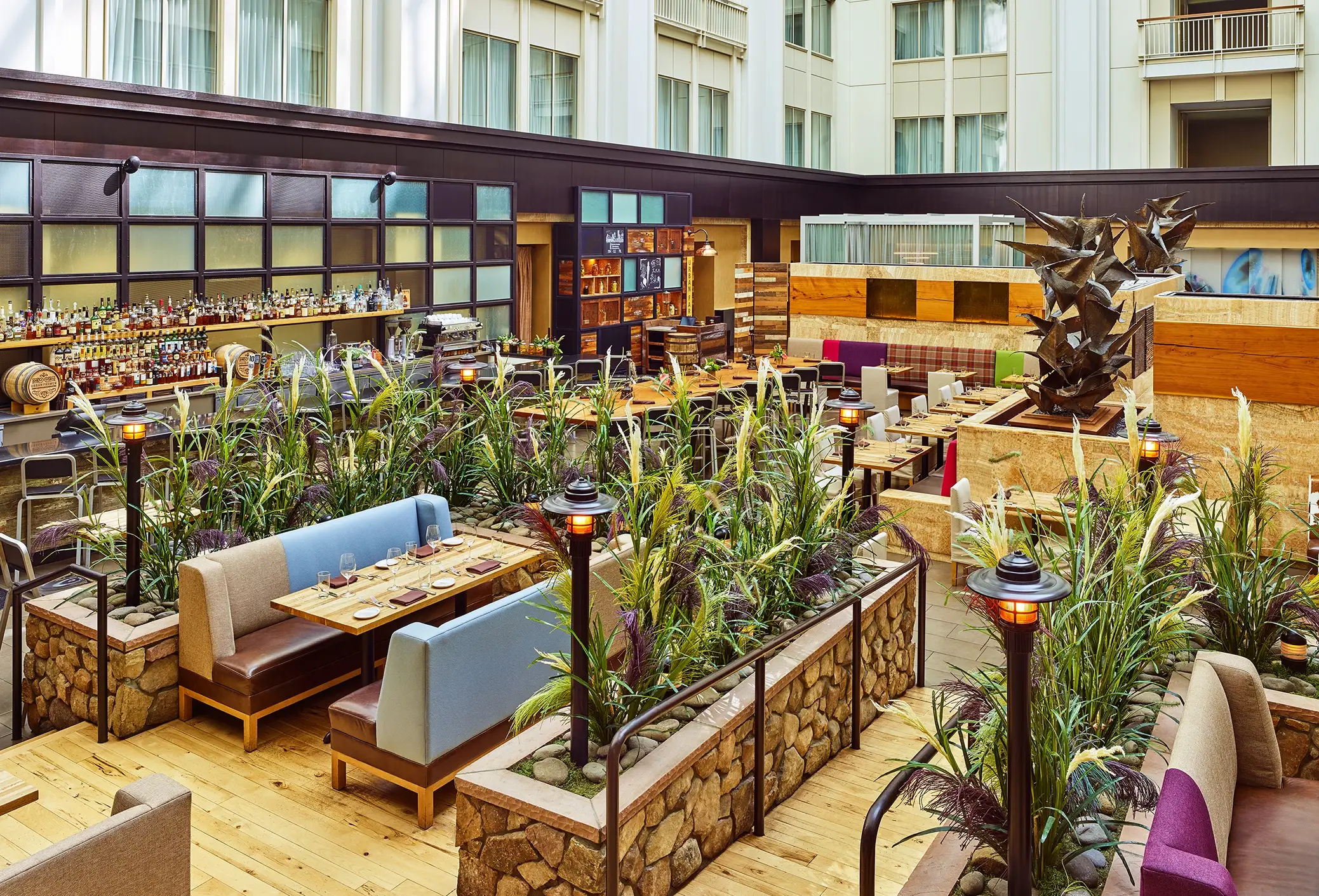 Elegant indoor atrium dining area at The Nines featuring stone planters, lush greenery, and a well-stocked bar.