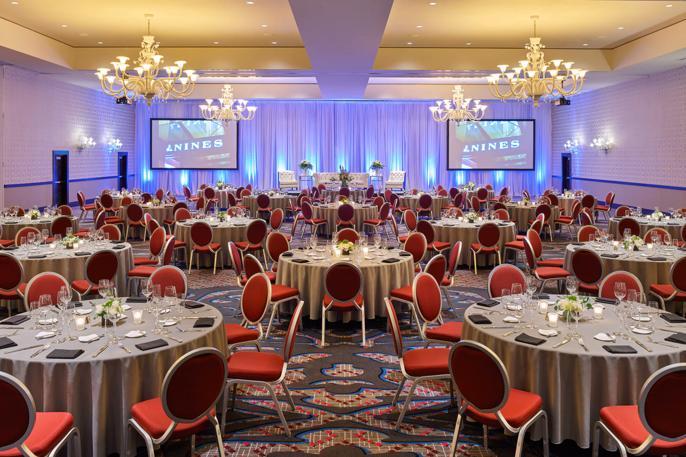 Elegant banquet hall at The Nines with round tables, red chairs, and purple uplighting.