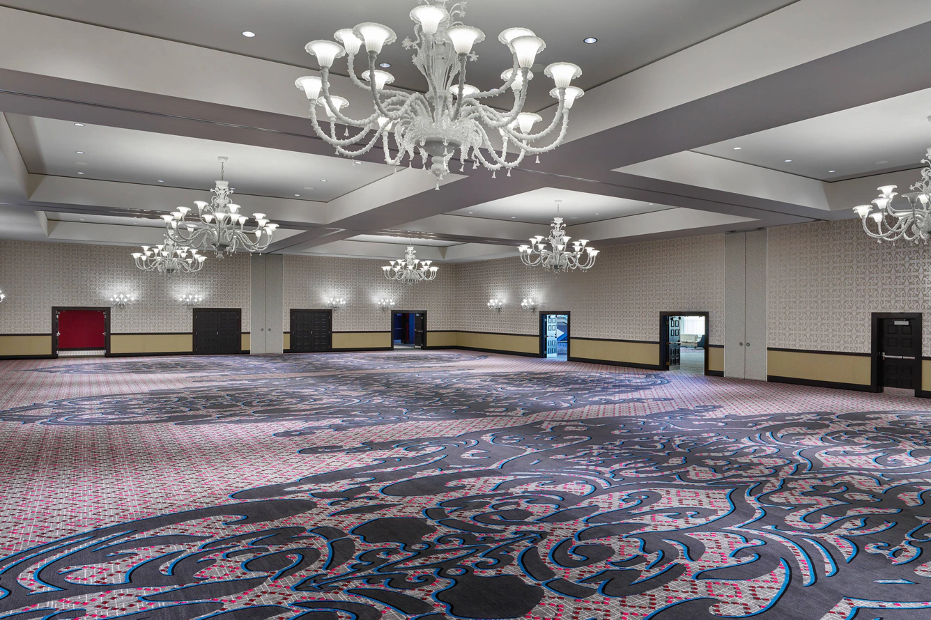 Spacious empty ballroom featuring patterned carpet and white chandeliers at The Nines