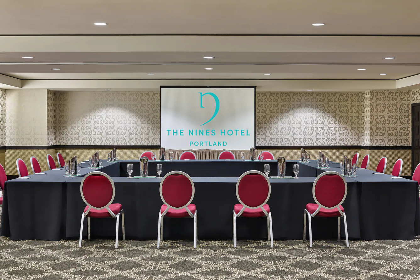 Conference room at The Nines Hotel Portland with U-shaped tables and red chairs facing a presentation screen.