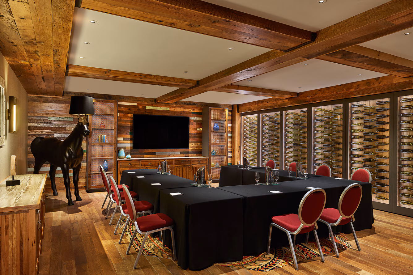 Elegant wine cellar dining room with black tables, red chairs, and a horse sculpture.