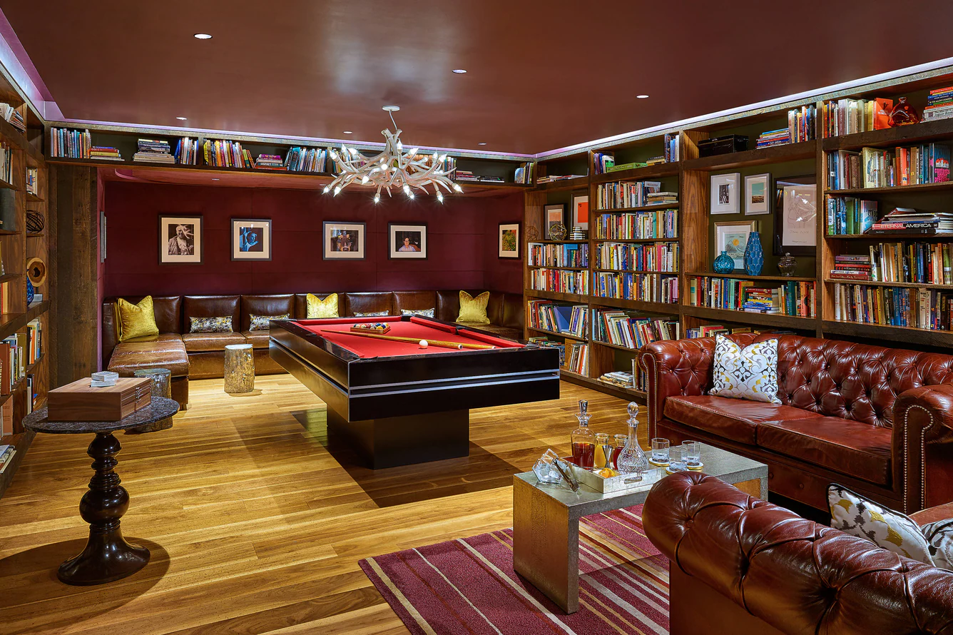 Luxury game room featuring a red pool table, leather seating, and floor-to-ceiling bookshelves.