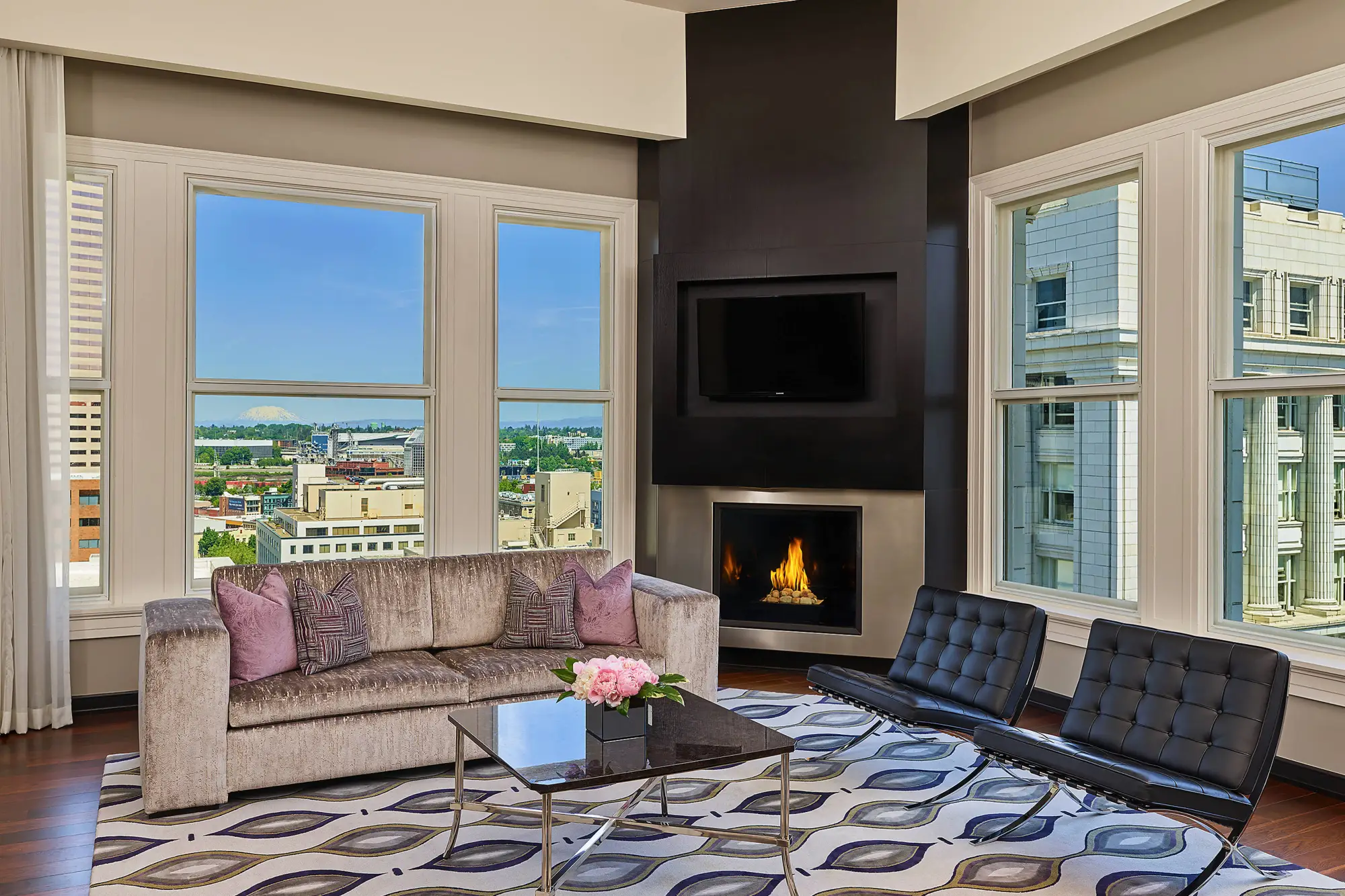 Luxury hotel suite living room with city views, fireplace, and modern furniture.