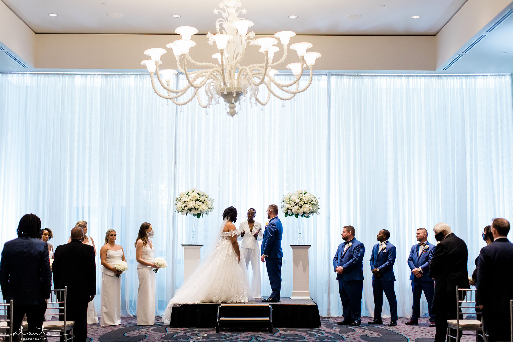 Wedding ceremony at The Nines with bride and groom at the altar under a chandelier.