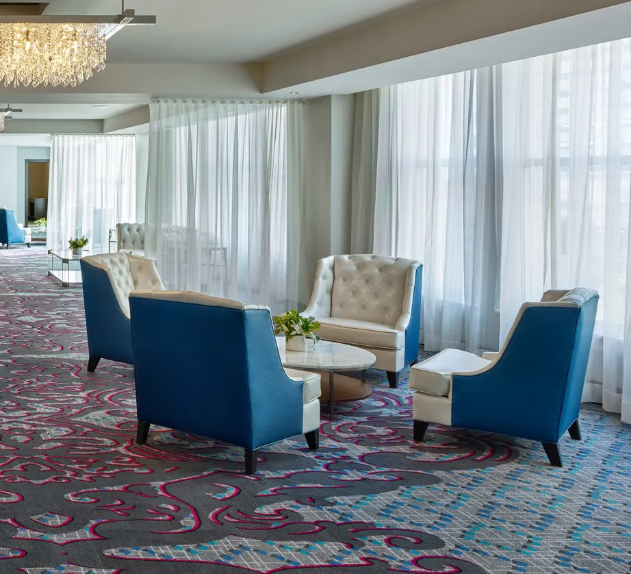 Hotel lounge seating area with blue and white armchairs around a coffee table on patterned carpet