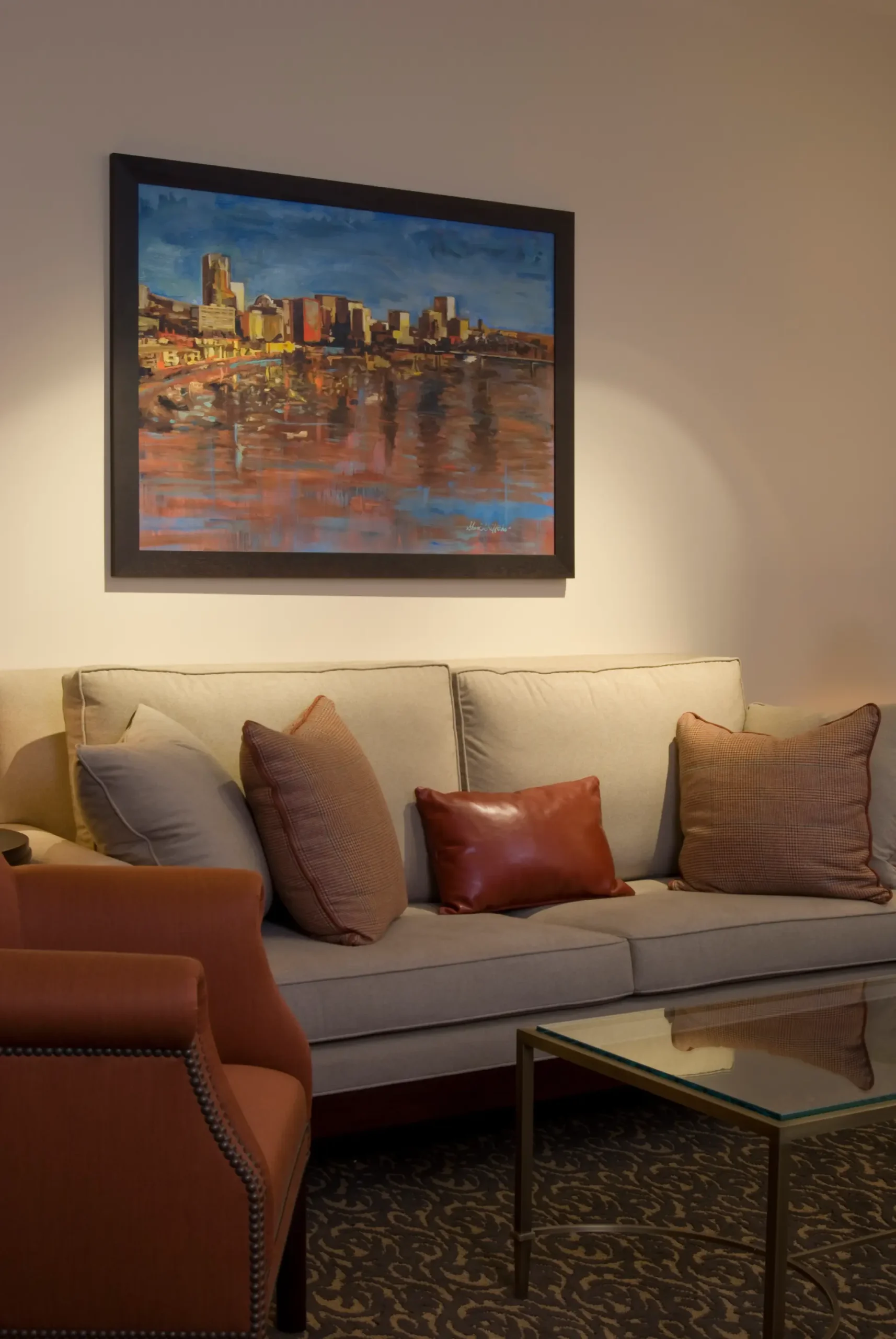 Lounge area with beige sofa, rust pillows, and cityscape painting