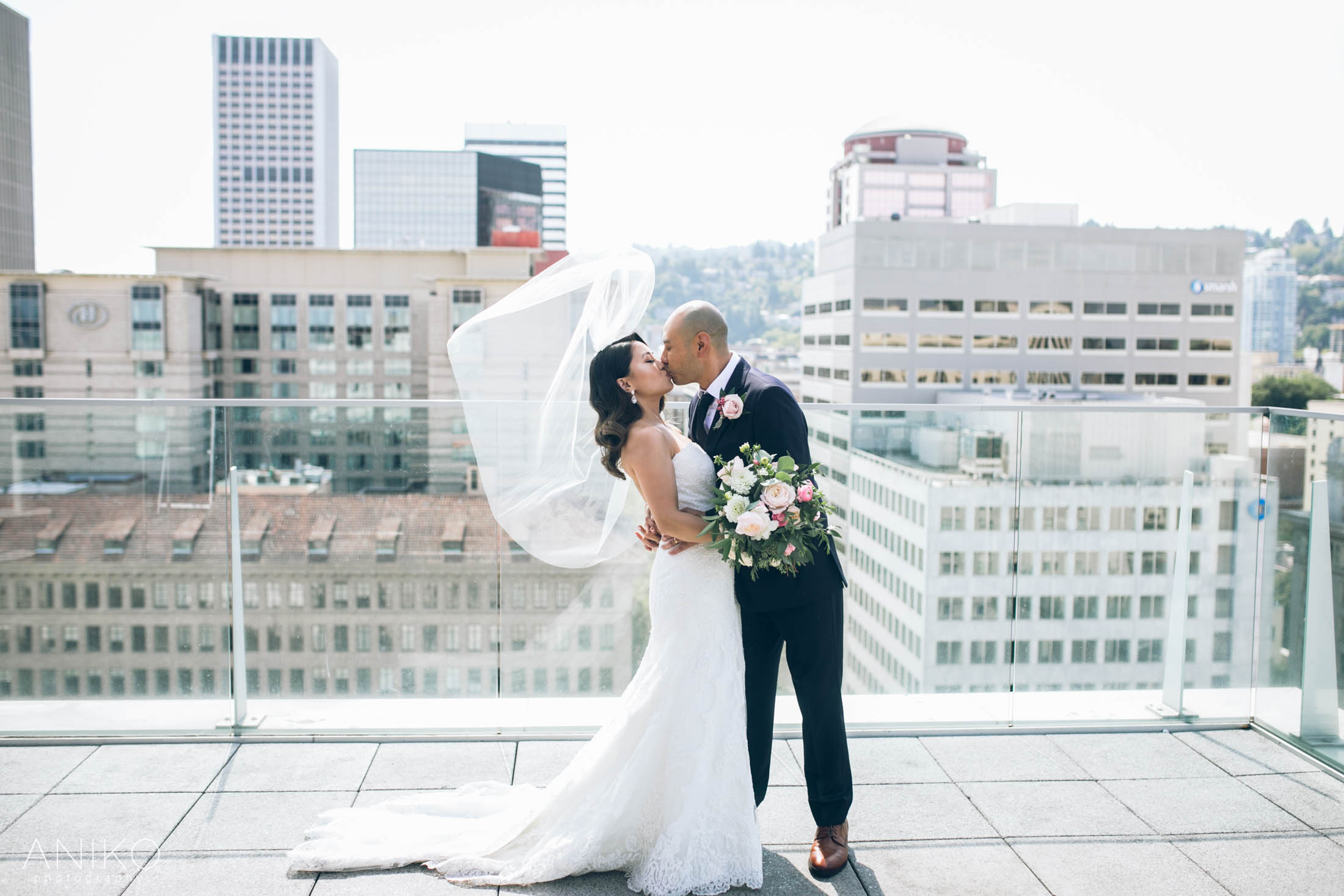 Bride and groom kissing on a rooftop terrace with a city skyline background