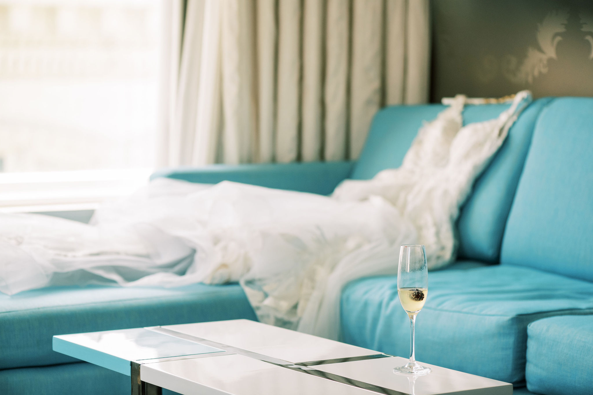 White wedding dress on blue sofa with champagne glass