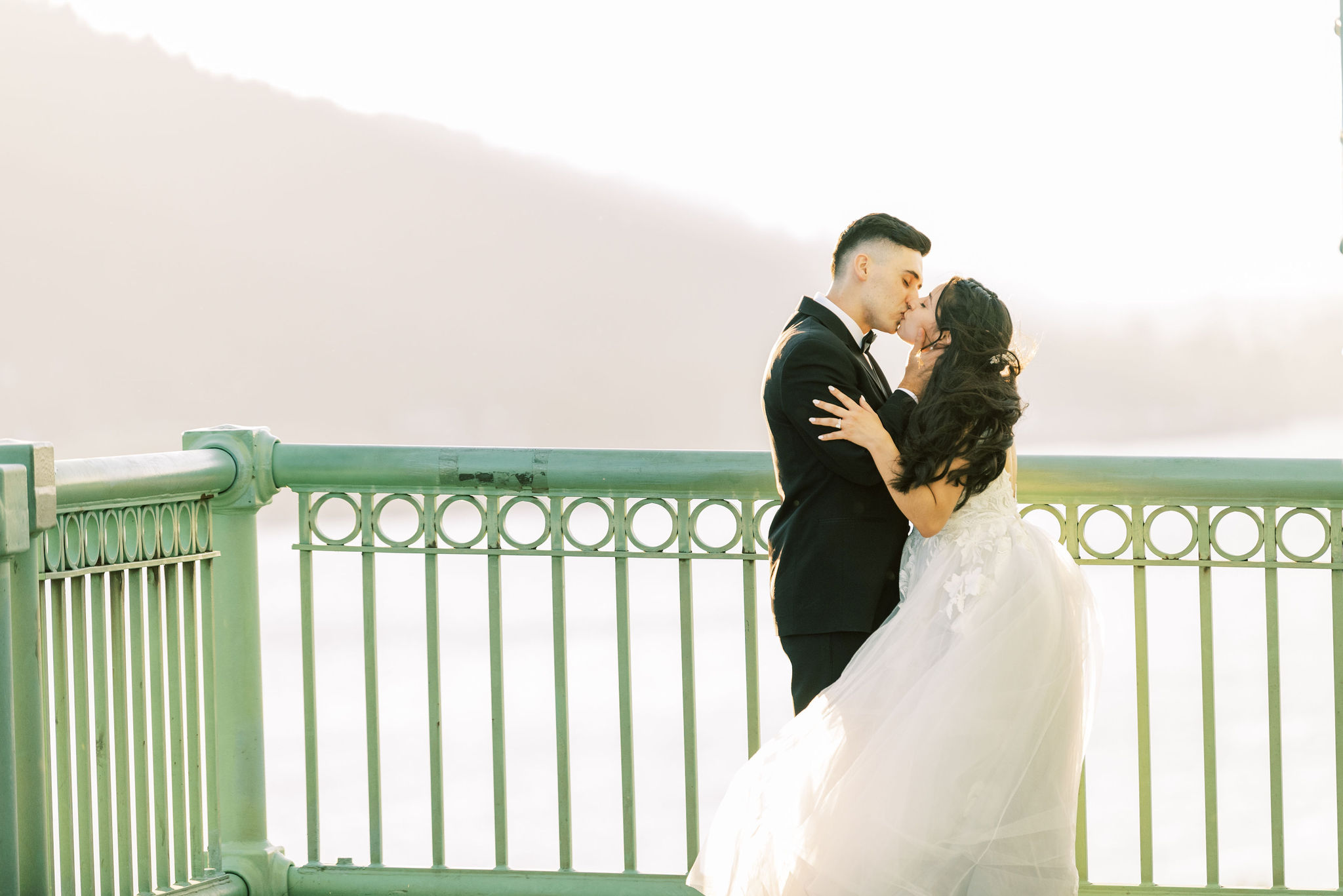 Bride and groom kissing on a bridge with a green railing