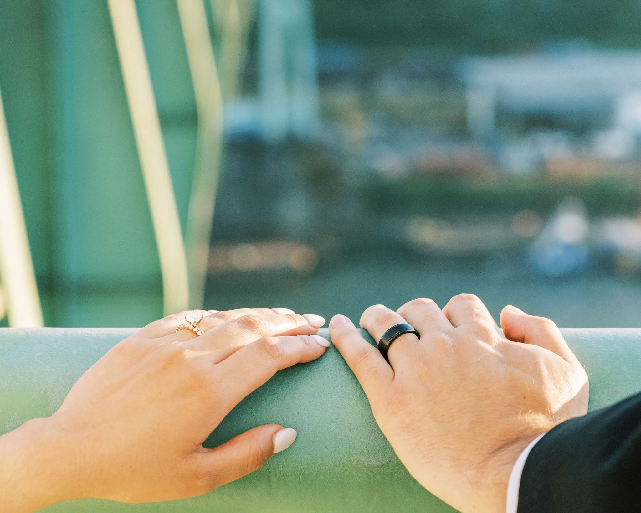 Close-up of a couple's hands resting on a railing, showing engagement and wedding rings.