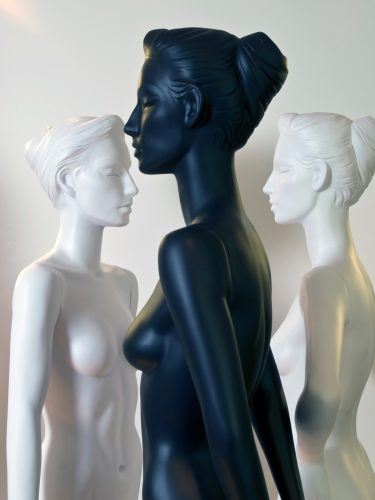 Three female mannequin busts, one black in profile flanked by two white figures facing inward.