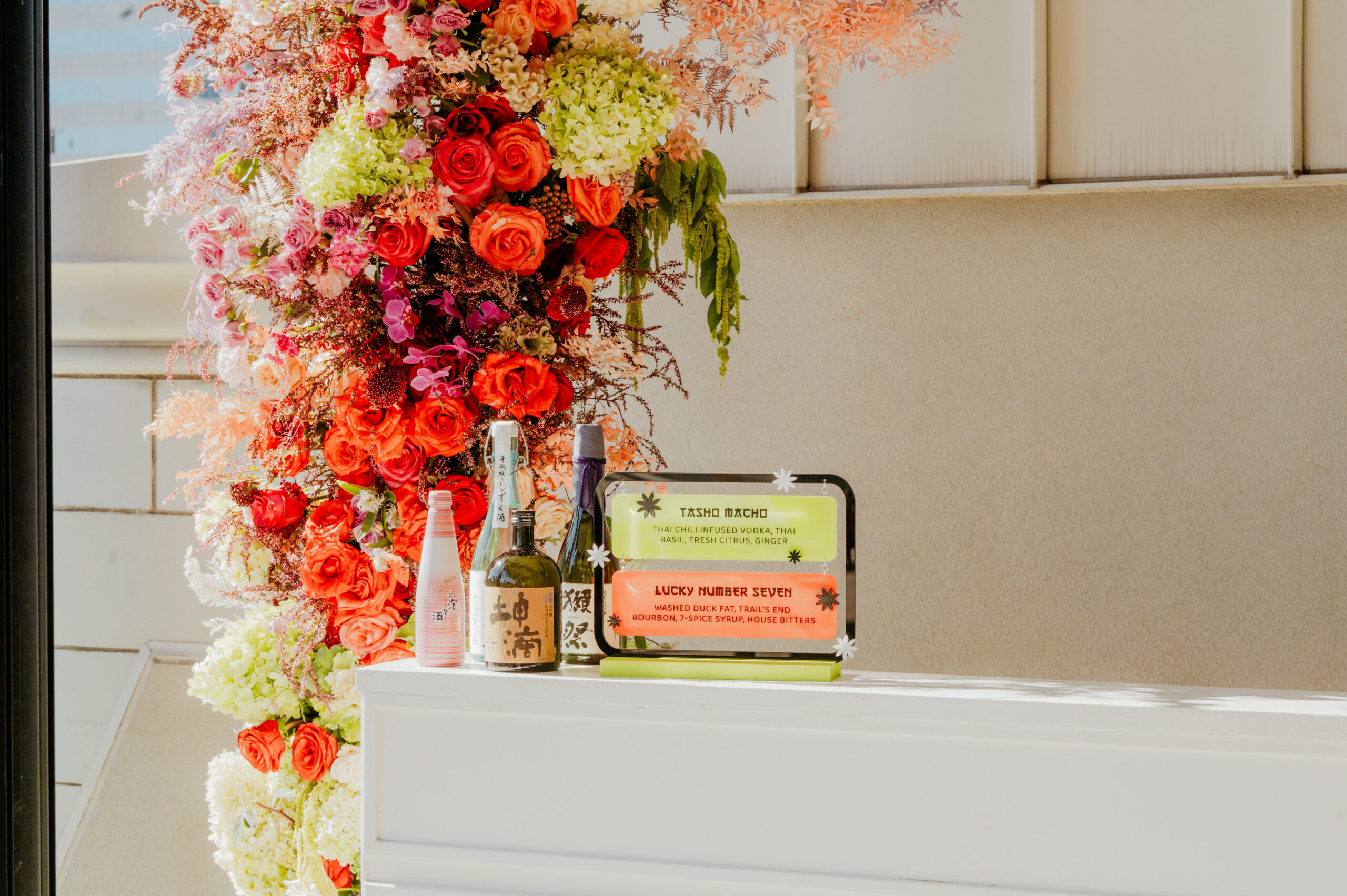 Cocktail bottles and menu cards displayed against a vibrant floral arrangement at The Nines.