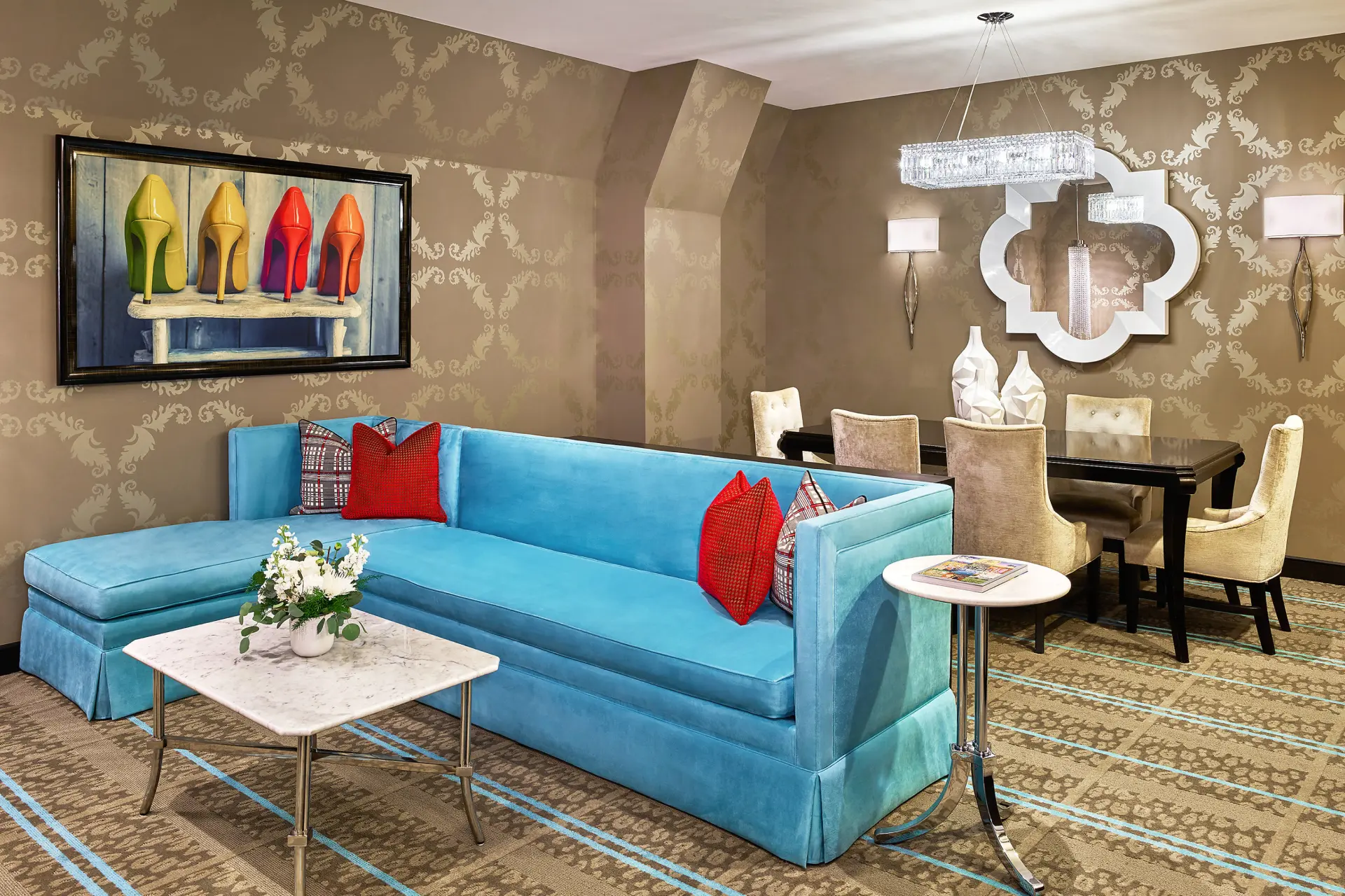 A chic turquoise sofa with red pillows sits near a dining table in a stylish Portland suites hotel room.