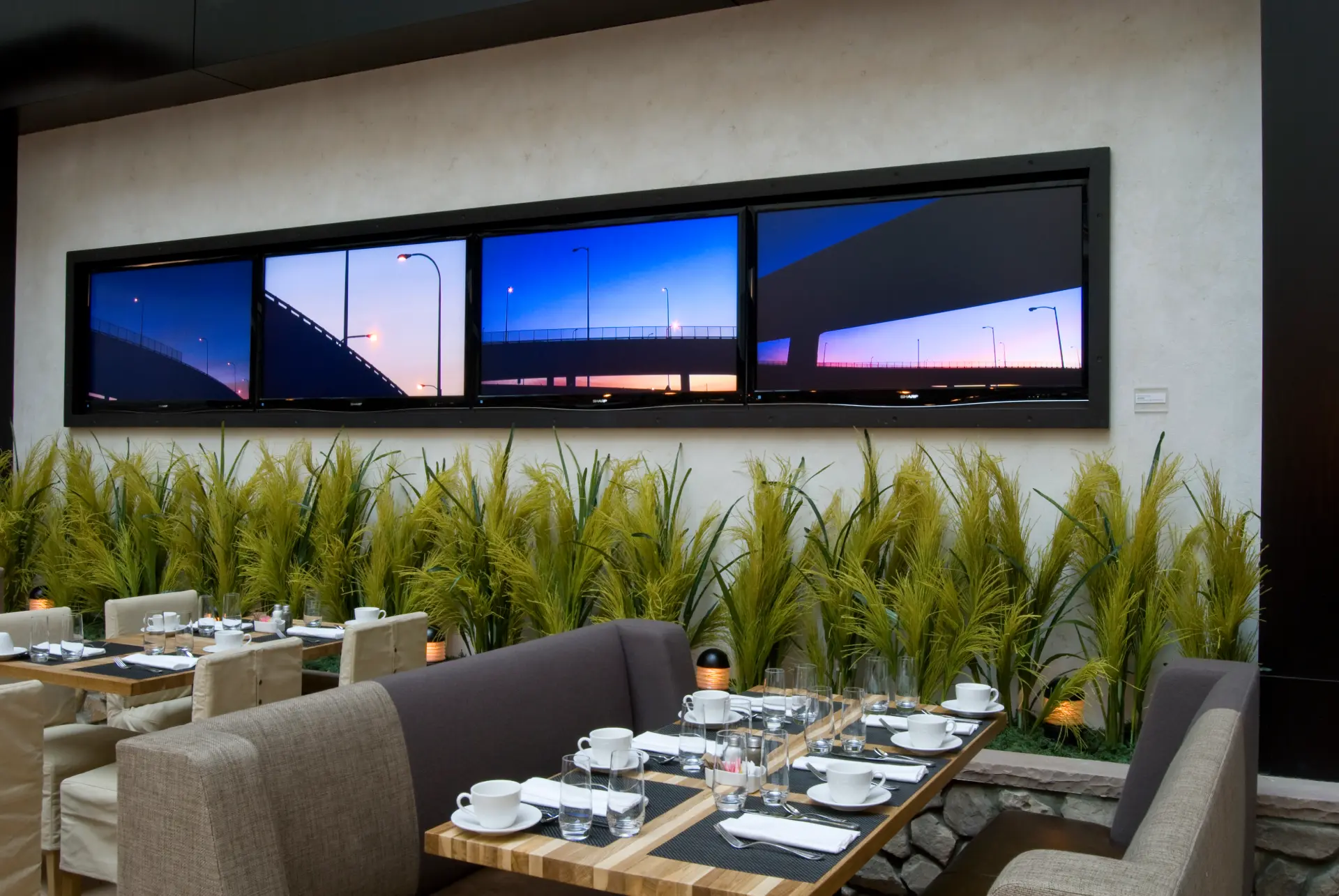 Restaurant dining area with booth seating, tables set for service, and a panoramic window view of a highway at dusk.