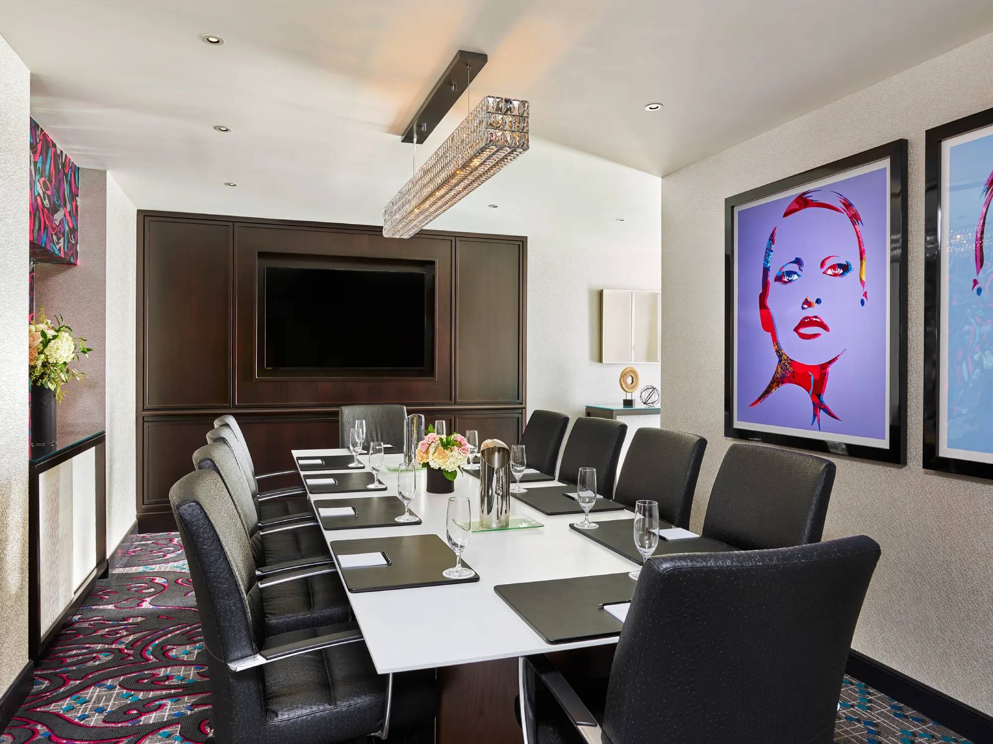 Modern private dining room with long white table, black chairs, and pop art portraits.