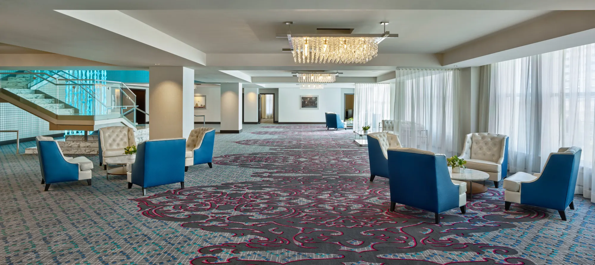 Elegant hotel lobby lounge featuring blue and cream armchairs, patterned carpet, and crystal chandeliers.